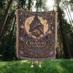 Moonlit bat woven blanket with purple flowers displayed in forest setting